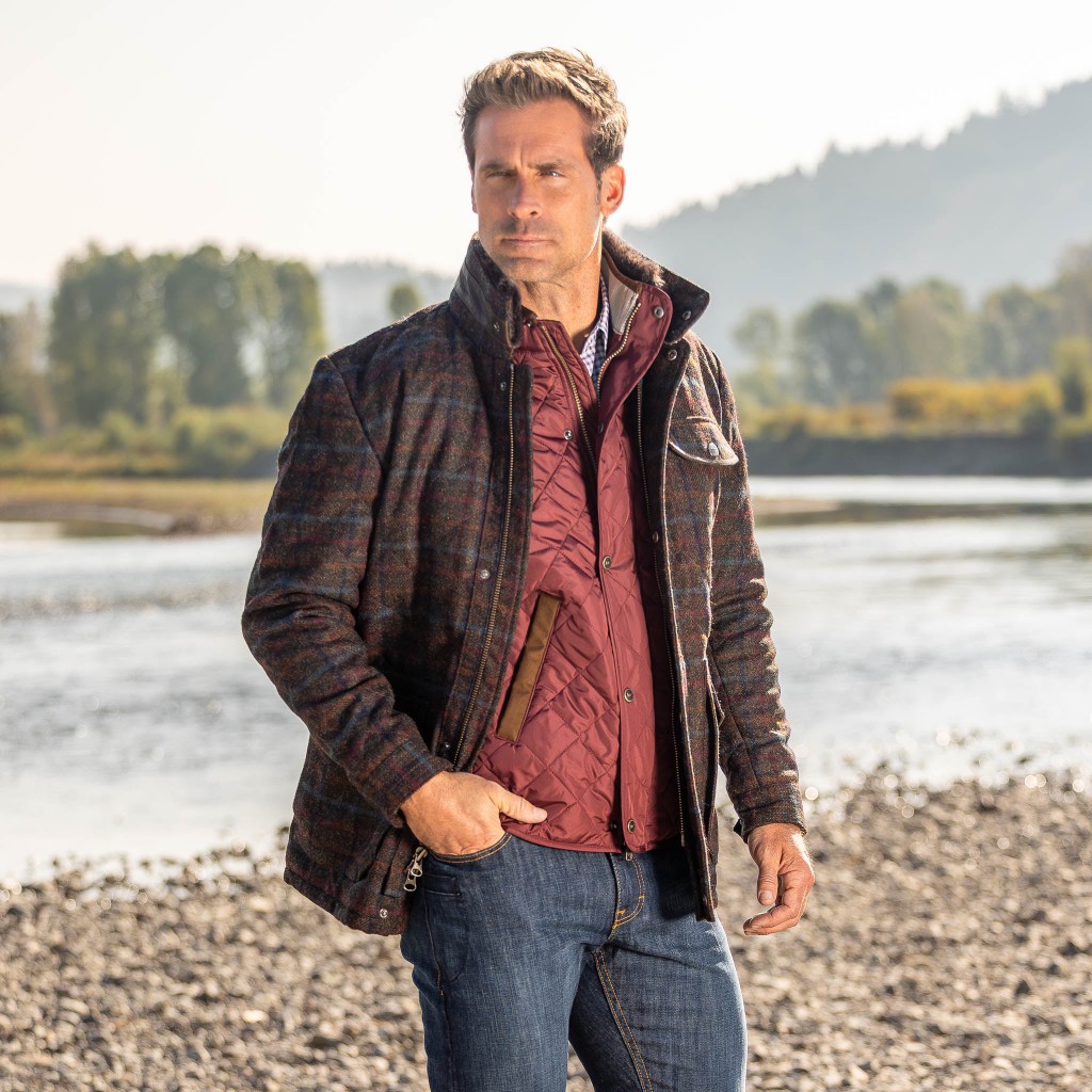 Man in a plaid field jacket and quilted vest on a riverbank